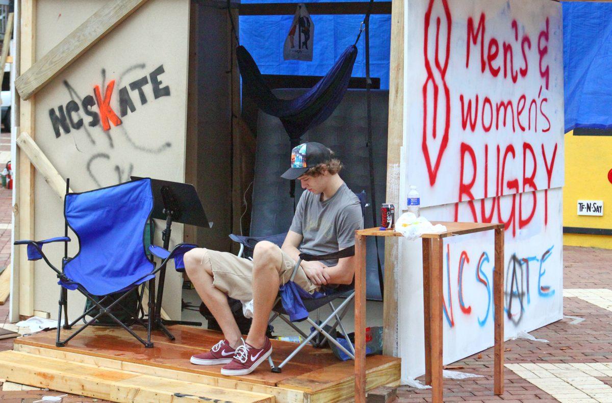 Representing NC Skate, Jeffrey Mickler, a freshman in aerospace engineering, sits on the porch of the shack NC Skate and the Rugby teams share after a shower passed on Tuesday. "The Habitat for Humanity shack is a great idea. It's a great way to raise money. There is a fact on every shack and tells people what it is about," Mickler said. Photo by Amanda Wilkins