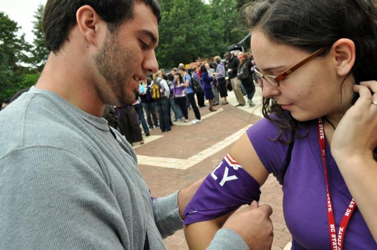 Kenny Hertling, a freshman in political science, helps Alicia Moreira, a junior in English and philosophy, with her purple ally band at the GLBT rally in the Brickyard Oct. 20. "My older sister is a lesbian and works on campus and I love her death and will support her every step of the way," Hertling said. Photo by Alex Sanchez