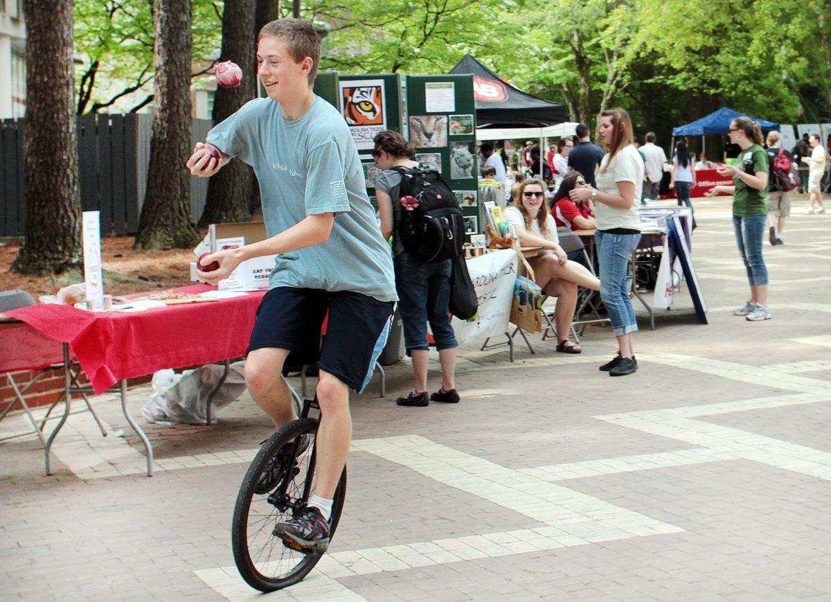 Jonathan Tufts, a sophomore in Biological Sciences, juggles three red onions while riding a unicycle in the Brickyard during the Earth Day Celebration Wednesday. The theme of the celebration was local food. Food vendors, educational organizations, and sustainable companies set up booths to educated and engage students and community members in local, sustainable practices. Photo by Katherine Hoke