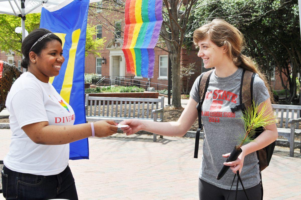 Nicole Benson, a junior in communication and member of the N.C. State GLBT Center, hands Brenna Garner, a sophomore in environmental technology, a sticker to show support of diversity. The event was a part of Ally Day that took place in Wolf Plaza Wednesday, April 9.&#160;