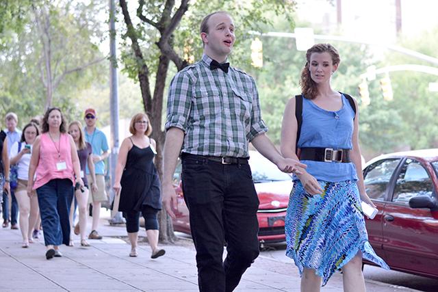 Actors David Godshall and Jess Barbour walk down Dawson Street in character with an entourage of audience members following close behind on Friday evening in Downtown Raleigh.&#160;