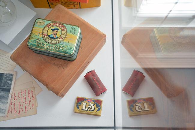 Cigarette boxes and a cigarette rolling machine are among the items encased in glass at the Smokes and Mirrors exhibit at the Gregg Museum on Hillsborough St. This exhibit showcases the personal items including cigarettes and cameras as well as the photographic works of the late John Menapace.