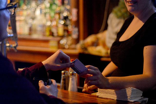 The night bartender at Mitch's Tavern checks the ID of a customer before serving alcohol. She said that Mitch's doesn't see many fake IDs and their usual crowd consists of mostly graduate students.