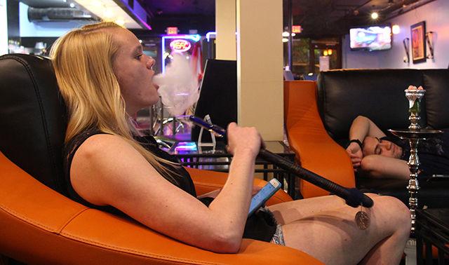 Courtney Weaver, junior studying business administration at Wake Technical Community College, takes a puff of hookah at the new bar Fuzion Cafe Lounge while Zack Khoueori, who works in Raleigh, rests while watching a soccer match on one of the couches.