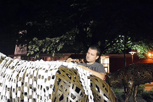 Chad Butts, a freshman studying engineering, decorates the wolf statue at Wolf Plaza Tuesday night after the candlelit vigil held in honor of Joseph Banks. Butts decorated the wolves with paper links that he stapled together himself, along with the help of a couple of his friends. "The links are meant to get people to think about the whole situation and how it could've been any one of us," Butts said.