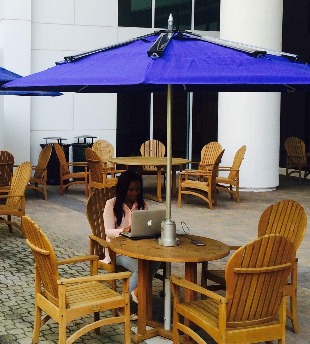 A student works outdoors under a ZON Powersol umbrella allowing her to charge her devices.&#160;Each umbrella has solar panels secured to the top which feed into a wire down the center of the umbrella. The wire connects to a lithium ion battery sitting on top of the table which can charge up to three USB devices at once.