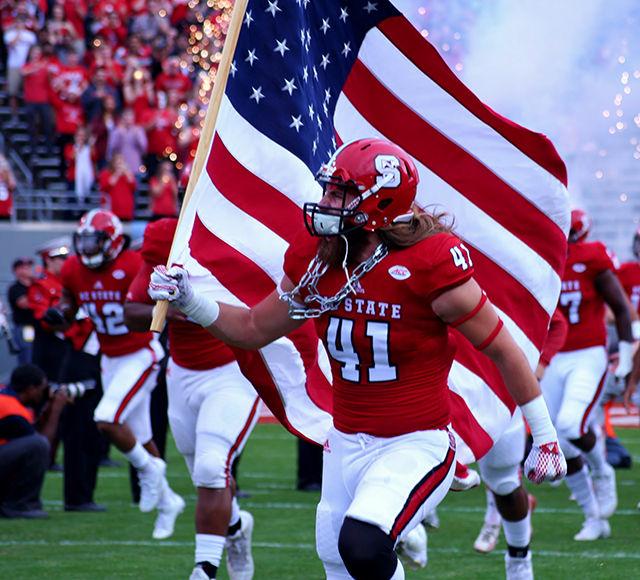 Redshirt junior Clark Eyers takes the field with the American flag in hand at Carter Finley Stadum on November 28. Opening ceremonies included a flyover by the Bandit Flight Team. The wolfpack lost the game 45-34