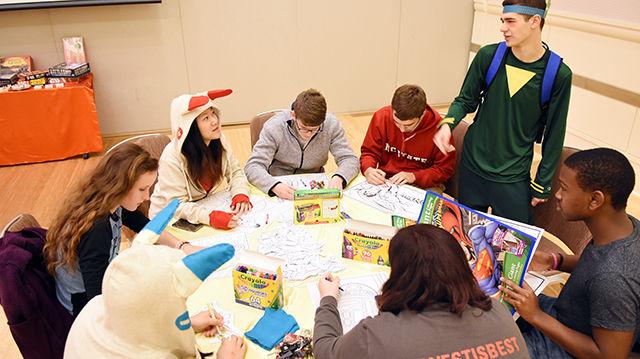 Francesco Trotta, standing dressed as "Iota" from the game Tearaway, a sophomore studying animal science, introduces himself to a group of students color pictures of comic book and movie characters at PackCon on Tuesday in the Coastal Ballroom of Talley Student Union.