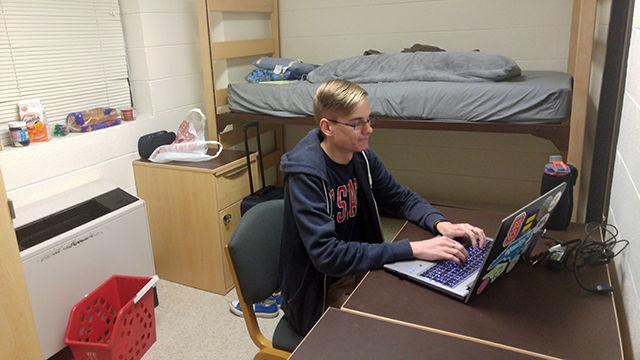 Case Cody, a junior studying accounting, works on his laptop in his emergency temporary housing in Wood Hall.&#160; Cody moved food, clothes, bedding, electronics, and other necessities in his suitcase until the power returns to Avent Ferry Complex.