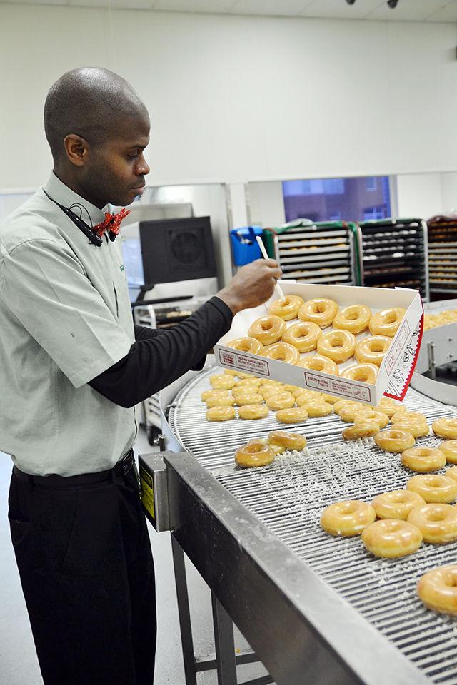 Andre Milton, the assistant general manager, picks a dozen Krispy Kreme doughnuts for a customer straight off of the production line Wednesday. These doughnuts have been freshly made for less than a minute or two by the time the customer has them in his or her hands.
