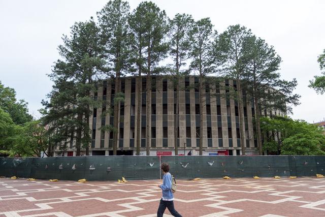 A student walks through the brickyard and looks at the fenced off Harrelson Hall on May 18, 2016. Harrelson Hall is in the process of being cleaned out and its contents recycled so that the building can be demolished. The building is scheduled to be demolished in June and the area cleared out by August when classes begin again.