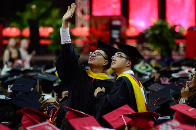 Two graduates wave at friends and family on May 7, 2016 in PNC Arena during the 2016 spring commencement. During the 2016 spring commencement 5,596 undergraduate degrees were awarded. The commencement also featured an address from Adm. Michelle Howard, the Navy's first female four-star admiral, a musical interlude by the Ladies in Red and a student address by Tatiana DeBerry, a graduating senior in criminology.