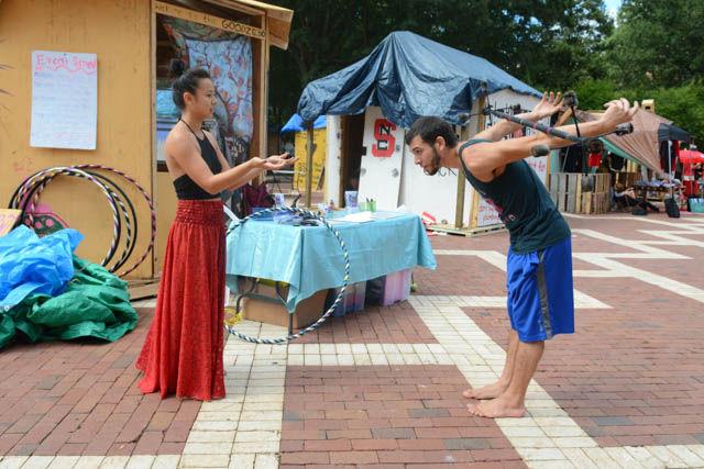 Phian Tran, a senior studying agriculture business management, watches as flow artist with Cirque Du Vol Gio Camacho shows her how to do do a barrel roll with a dragon staff in the Brickyard during the last day of Shack-a-Thon Friday. The Good Club's shack called the "Goodzebo" had guest performing artists throughout the week to come out to promote both Cirque du Vol and Celestine Movement Arts. According to club officer and freshman studying social work Sara Darwish, the Good Club is about spreading happiness and wellness around campus. The annual fundraiser to raise money for Habitat for Humanity included 26 shacks built by representatives of various student organizations on campus.