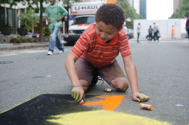 Jaden Cooper, 10, draws a sunset falling behind mountains at this year's SPARKcon on Fayetteville Street in downtown Raleigh on Sept. 16. The street painting squares are five feet wide by five feet tall.