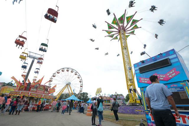 A fairgoer stands at a ticket booth while the new chairlift The State Flyer and the swing ride called The Vertigo are in operation at the 149th Annual N.C. State Fair Friday, Oct. 21 2016. The annual fair featured many rides, a variety of food, games, prizes, animals and other attractions.