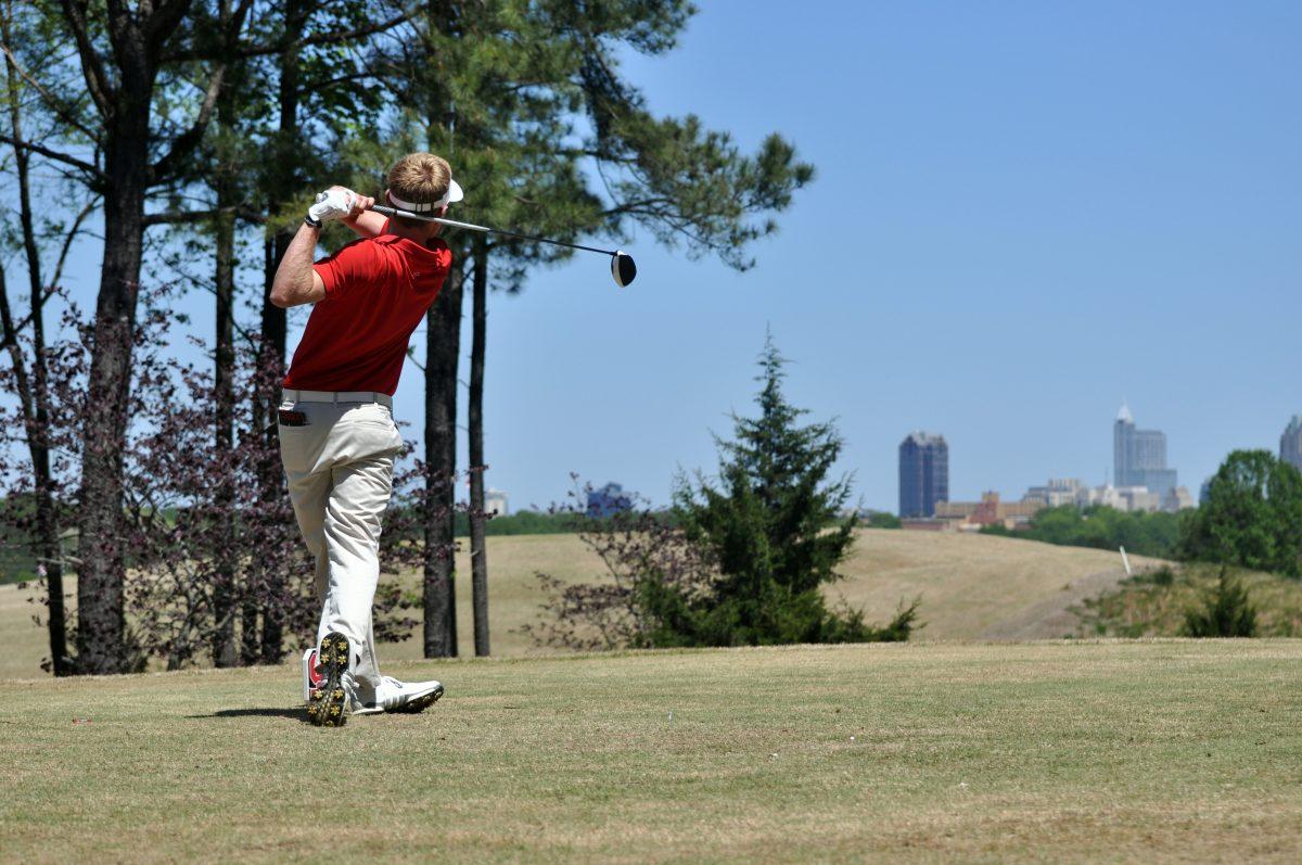 David Cooke, a senior watches his drive with the Raleigh skyline in the background. He set the Lonnie Poole Golf Course record with a score of 62 on the first day of the tournament. The tournament was held from Saturday, April 17, through Sunday, April 18, 2016.