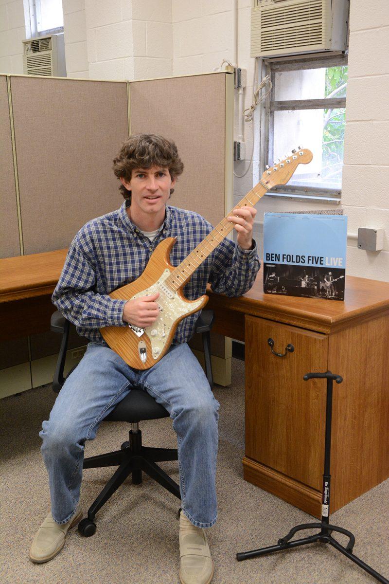 William Boone, adjunct professor of music in NC State's Music Department, sits with his guitar in front of a Ben Folds Five album in his office in Broughton Hall on March 22. Boone teaches MUS 211, Rock: 1980s-present, and is in his fourth year of teaching at NC State. This past fall semester, Boone's class welcomed Robert Sledge, the bass player for Ben Folds Five, whose album is beside Boone, as a guest speaker to talk about the local music scene in the 1990s.