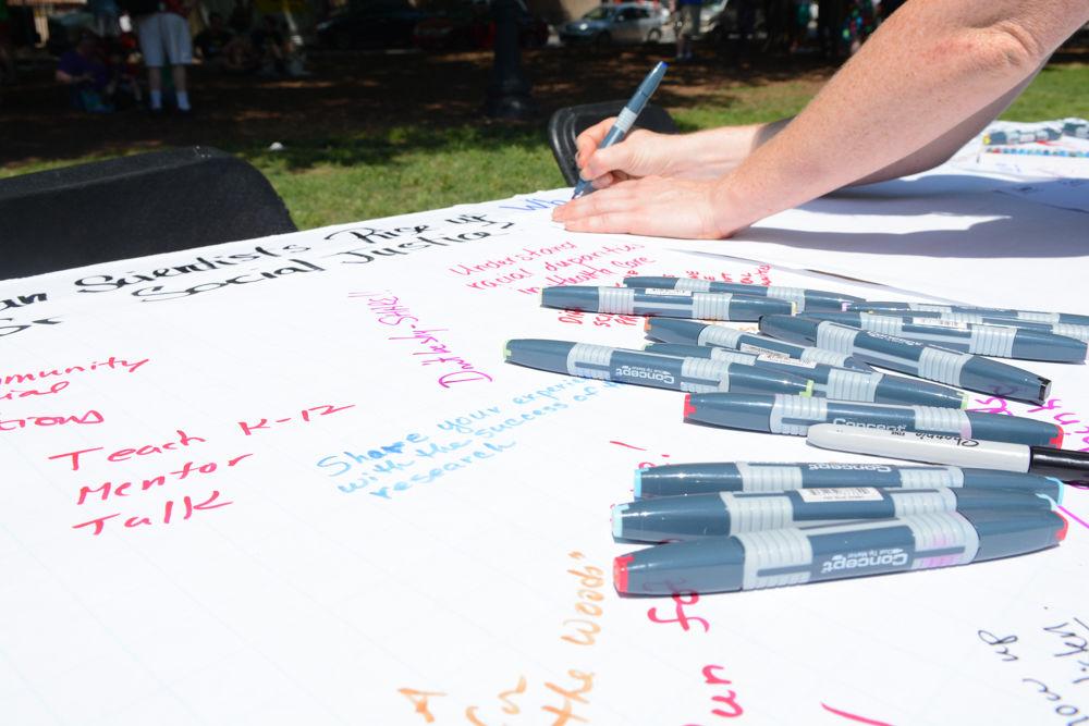 A volunteer at one of the tables at the community science fair held in Moore Square on April 22, 2017 writes a new question for citizens to answer. The table had poster paper with thought-provoking questions, such as "Can scientists rise up against social justice?" and citizens had the opportunity to write down their responses. The science fair was held as part of the first ever held Raleigh March for Science, one of the many science marches that took place across the world on Earth Day.