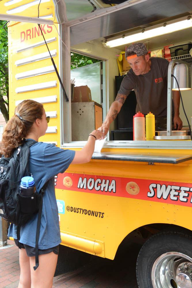 Elizabeth Day, a sophomore studying business administration, receives a donut from Daniel Horn, an employee working the Dusty Donuts food truck at Wolf Plaza on April 28. Dusty Donuts was one of multiple food trucks on campus during last day of classes festivities, which included food, games and opportunities for students to relax and celebrate before finals.