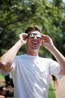 Nolan Joyce, a second year studying engineering, looks at the sun next to the Wolf Ears on Monday. Thousands of students gathered around the NC State Brickyard to enjoy eclipse festivities. Eclipse glasses were handed out to students and families attending the event.