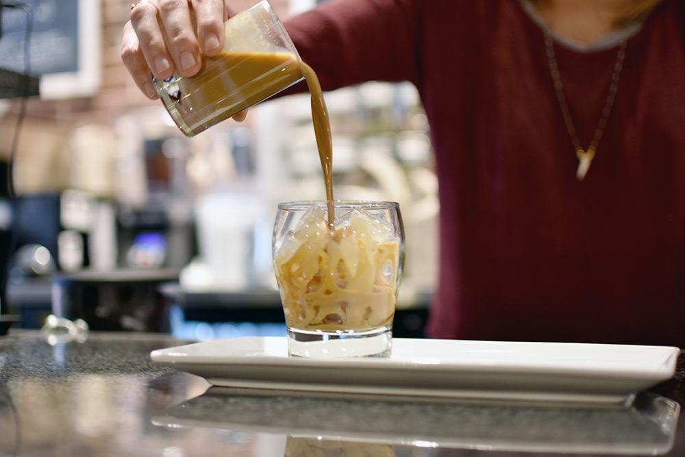 After stirring the contents of a glass, a barista for Liquid State pours a Thai iced coffee made with sweetened condensed milk and espresso over ice. Liquid State is an independent coffee shop that also serves beer and wine.