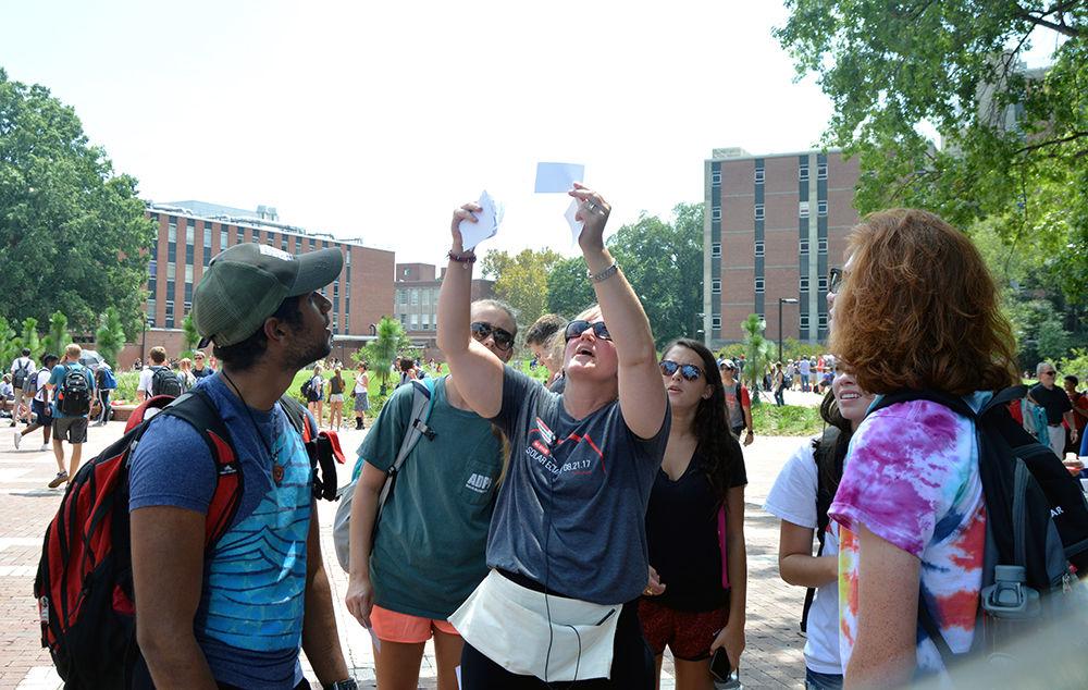 Katherine Titus-Becker the director of the Women in Sciences and Engineering Village shows a group of students how to use the pinhole projectors during the Solar Eclipse festivities at the Brickyard on Monday, Aug. 21.