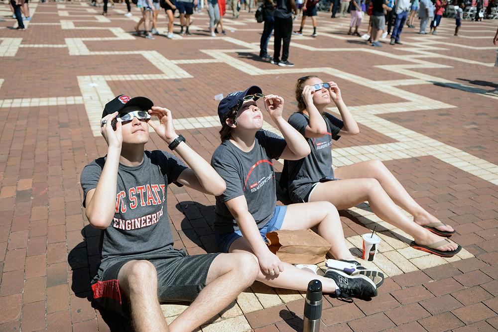 Stephen Hudson a first-year aerospace engineering student, Caroline Mason a first-year biology student and Kaitlyn Tiffany a first-year life sciences student view the eclipse through their glasses in the Brickyard on Monday, Aug. 21. This was the first time in 99 years a total solar eclipse could be viewed over the entire continental United States. The College of Sciences hosted a celebration full of science activities and safe ways to view the eclipse.