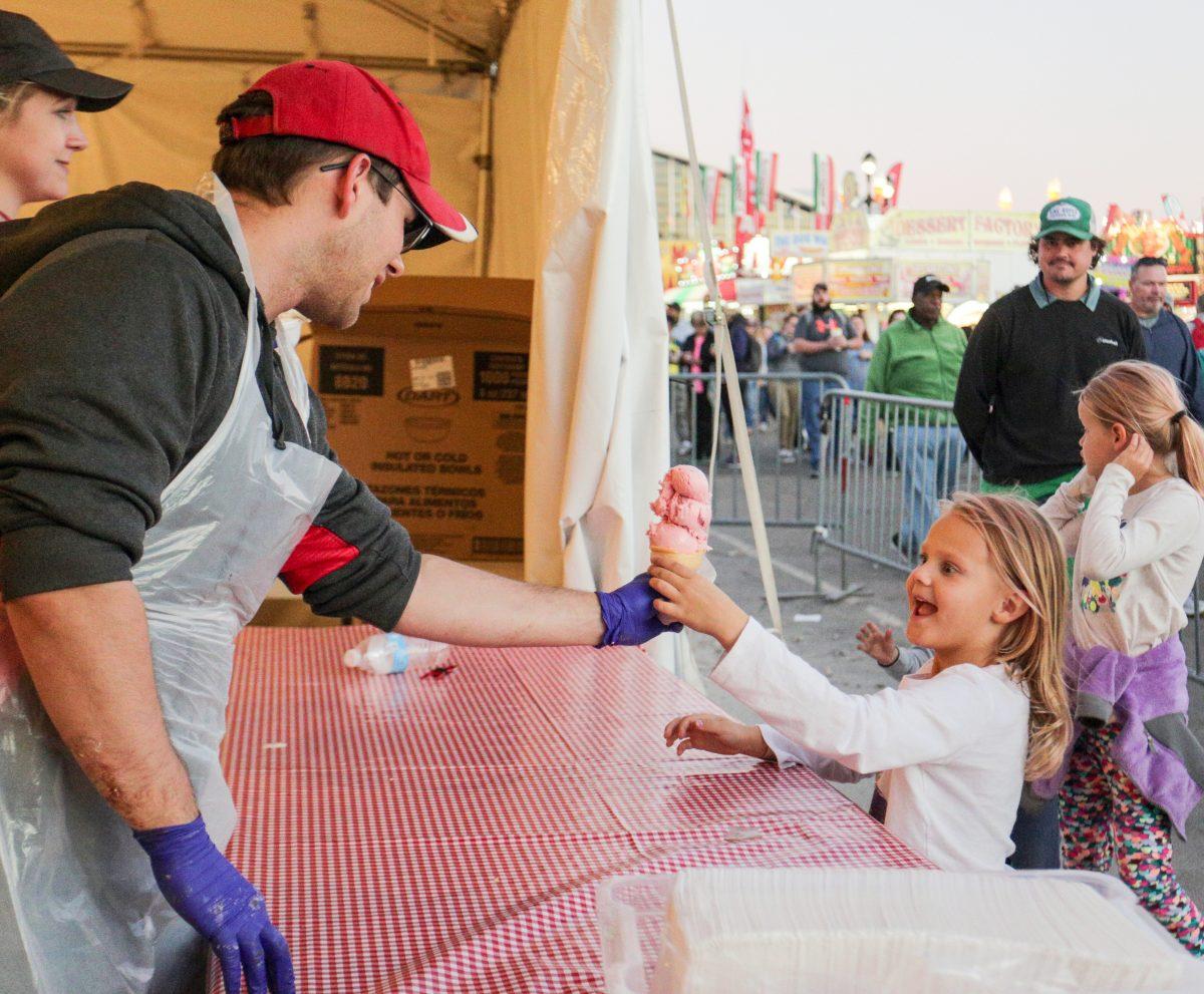 Mike Draper, a first-year graduate student studying food science, hands a triple scoop of Howling Cow ice cream to 6-year-old Kennedy Cape on Tuesday. The food science club sells hundreds of gallons of ice cream each year at the NC State Fair as their biggest fundraiser. The Fair runs from Oct. 12 to 22.