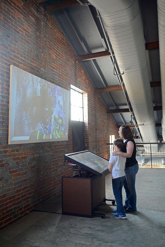 Jake Bower, age 10, interacts with a piece called "Synthetic Antibiotics" alongside his mother, Emili Bower, at Transfer Co. Food Hall in Raleigh on June 15. Transfer Co. Food Hall is currently hosting an exhibit called "Invisible Worlds", which is a collaboration project between The Leading Strand and NC State meant to expose observers to science-based works of art.