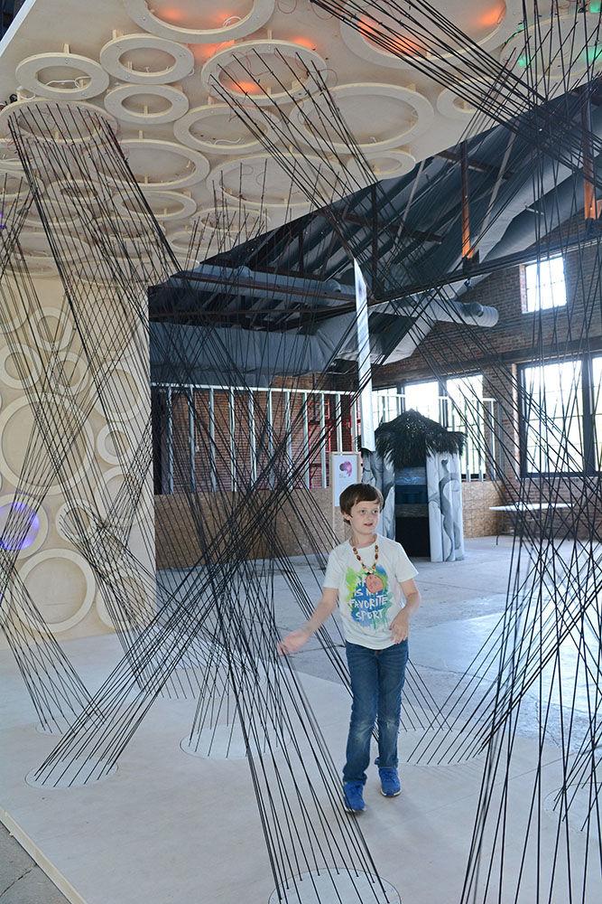 Jake Bower, age 10, travels through a piece called "Force Networks", pulling cords to generate different colored effects at Transfer Co. Food Hall in Raleigh on Friday, June 15. "Force Networks" is part of an exhibit called "Invisible Worlds", a collaboration project between The Leading Strand and NC State meant to expose observers to science-based works of art.