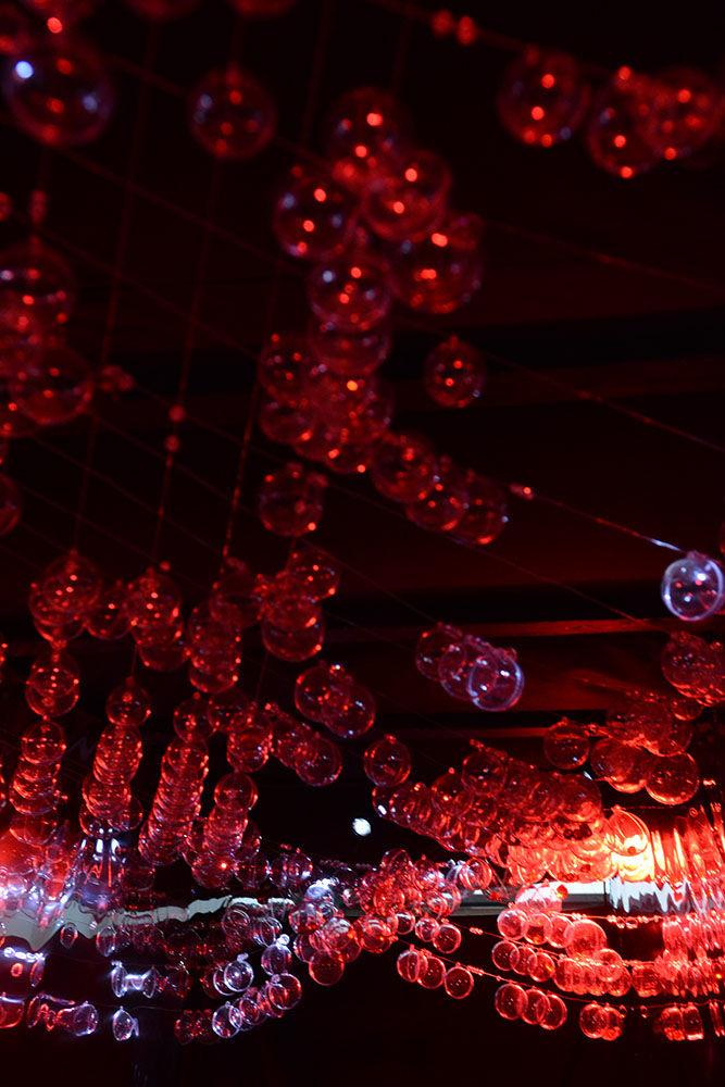 Multiple orbs illuminated with red light lead observers into the "Invisible Worlds" exhibit piece called "Dark Matter". "Dark Matter" is meant to illustrate "how the distortion of light can reveal the presence of dark matter". The exhibit, a collaboration between NC State and The Leading Strand, is open to the public through the month of June at Transfer Co. Food Hall in Raleigh.