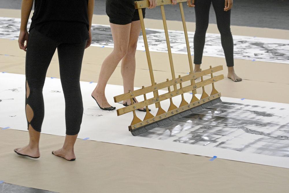 Dancers add a finishing coat of paint to their composition of "John Cage's STEPS" with a large paint brush on Wednesday, Sept. 19 in Carmichael Gymnasium. "STEPS" involved dancers stepping in black paint and tracking their footprints on a long piece of paper along to the occasional sounds of instruments.