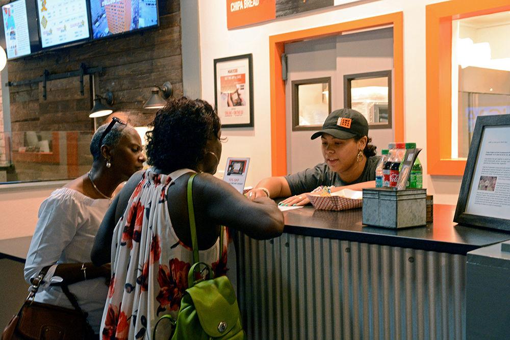 Makayla Anderson, an employee with Makus Empanadas, shows Clayton resident Brenda Irwin and Raleigh resident Celery Alston a menu at the Morgan Street Food Hall on Sunday, Sept. 9. Irwin said she ordered "the three empanada special" from the vendor.