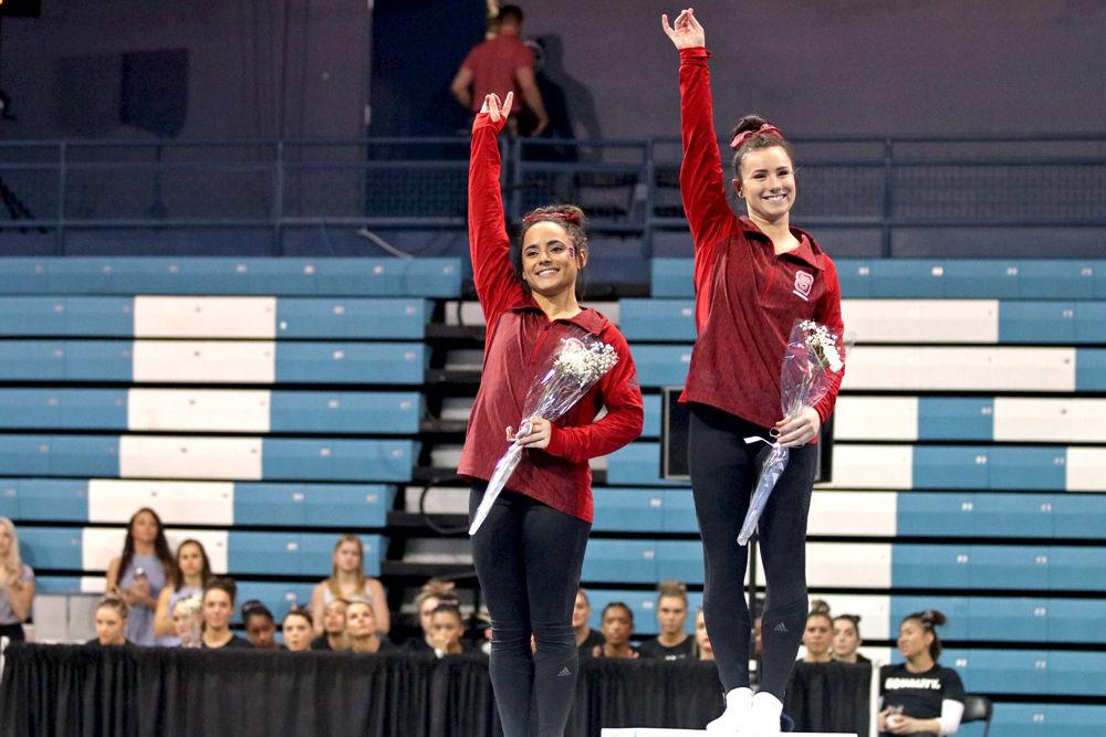 Senior Caitlyn Fillard and junior Drew Grantham throw up their wolfies to the crowd as they are presented 1st and 2nd place in the All-Around competition on Friday, Jan. 25 in Carmichael Arena. NC State defeated UNC-Chapel Hill with a close score of 195.200-194.650.