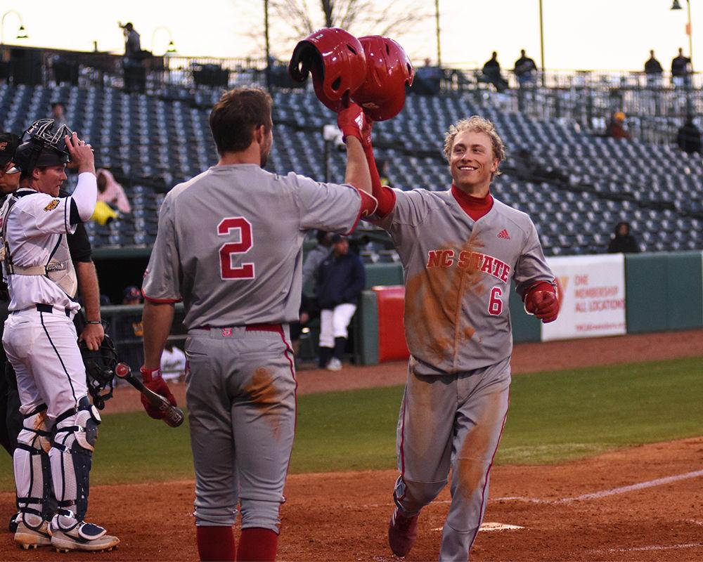 Freshman infielder Vojtech Mensik knocks hats with sophomore outfielder Jonny Butler after the former earned a run on Wednesday, March 27, at First National Bank Field. The Wolfpack beat the Aggies 12-3.
