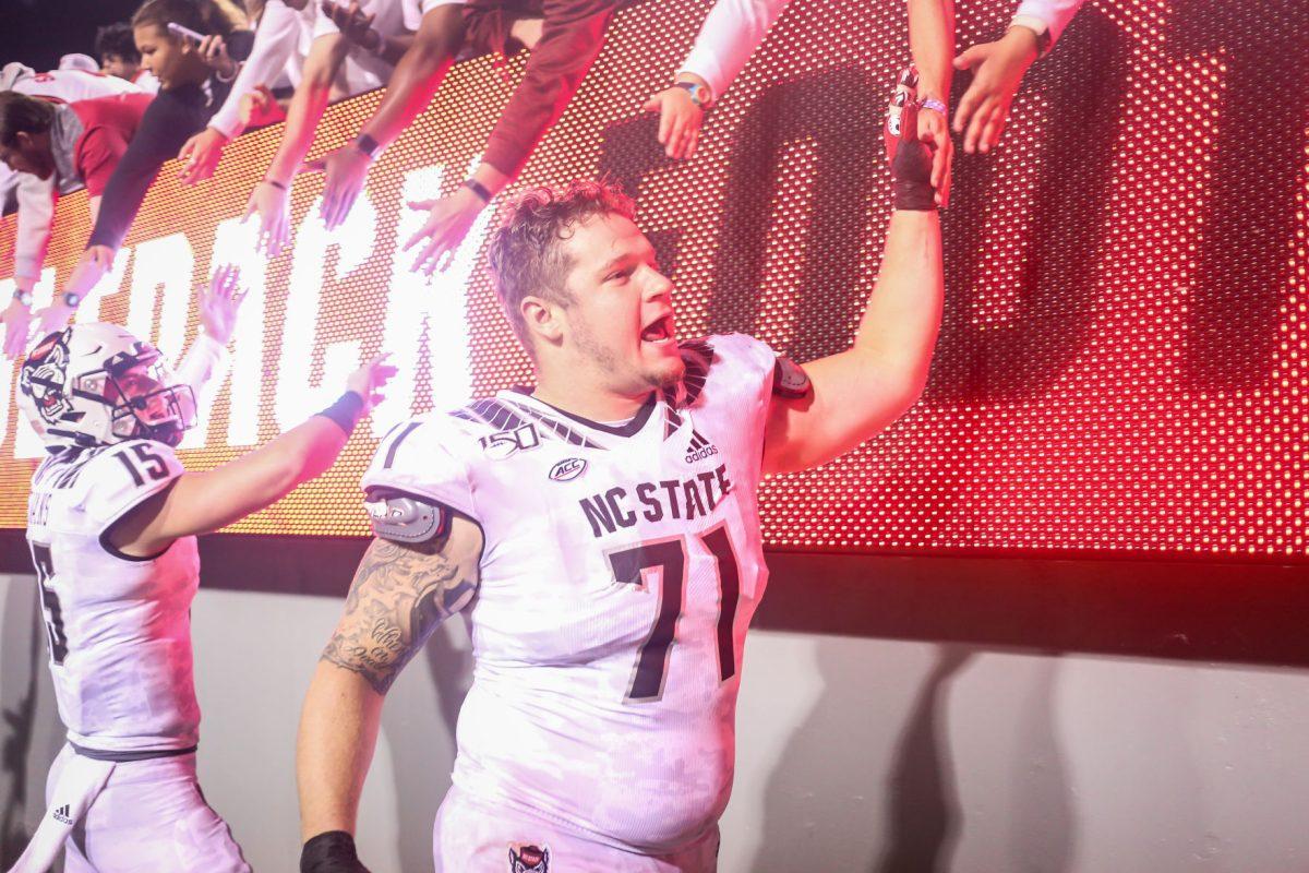 Redshirt junior offensive guard Joe Sculthorpe celebrates the team's win over Syracuse by high-fiving fans in front of a 'Wolfpack Football' sign, along with teammate freshman quarterback Ty Evans. NC State hosted the Syracuse Orange on Thursday, October 10, 2019. NC State won the game 16-10.