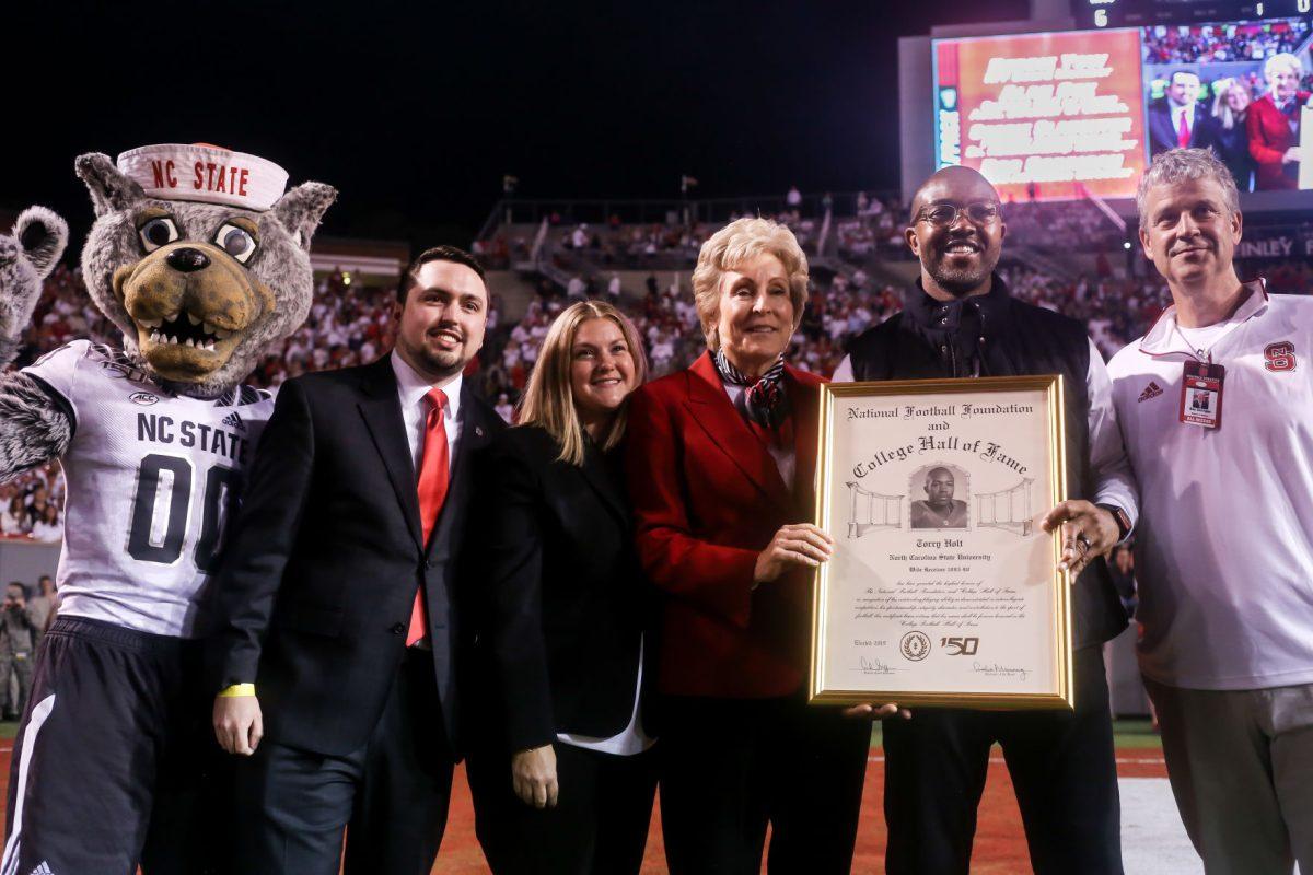 Former NC State wide receiver Torry Holt celebrates his induction into the College Hall of Fame alongside former and current Athletic Directors Debbie Yow, left, and Boo Corrigan, right, during a stoppage in play of the Wolfpack's 16-10 home win against the Syracuse Orange on Thursday, October 10, 2019. Holt will be inducted on Dec. 10, 2019, after a distinguished career at NC State where he still holds numerous ACC records, and an 11-year career in the NFL with multiple All Pro seasons and a Super Bowl championship. His senior season of 1998, he totaled 1,604 receiving yards, and his average of 145.8 yards per game is over 20 yards better than any other receiver in ACC history.