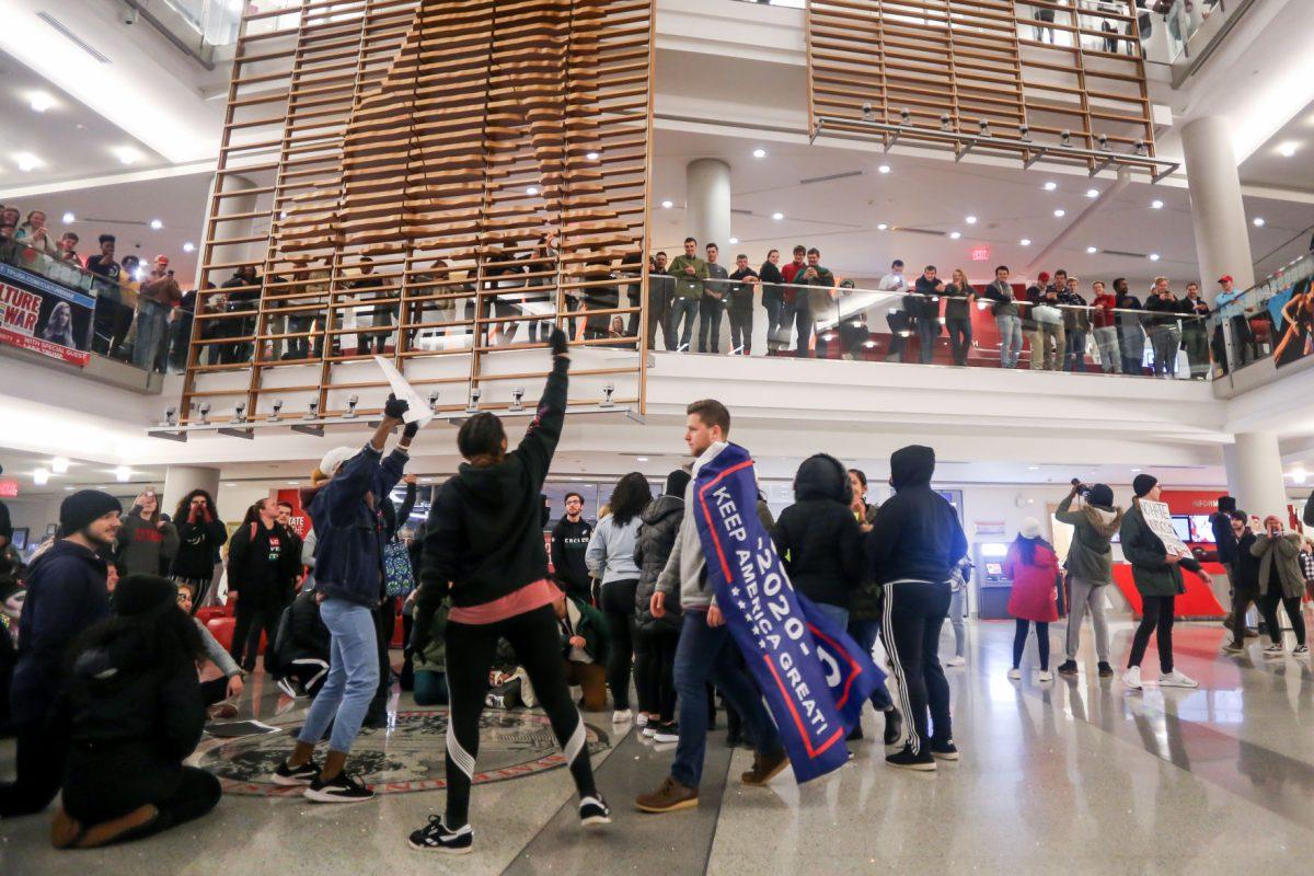 Jakob Sealock, center, a freshman studying electrical engineering, wears his Trump 2020 flag as a cape while he walks through a group of chanting protestors on his way to a Turning Point "Culture Wars" event in Talley Student Center on Wednesday, Nov. 13, 2019. "It's interesting, honestly," he said about the protestors. "I don't agree with them, obviously, but they have the right to do this."