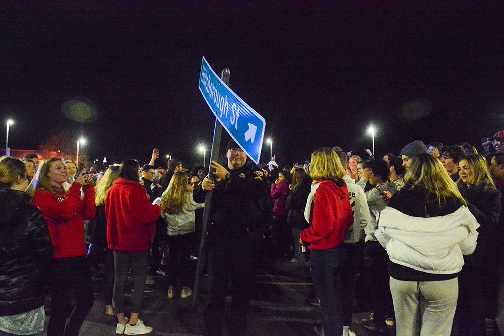 A raleigh police officer carries away a Hillsborough sign after it was torn down by students rushing the Bell Tower after the 88-66 win over Duke on Wednesday, Feb. 19, 2020. Hillsborough Street flooded with Wolfpack fans in support of the men&#8217;s basketball team win.