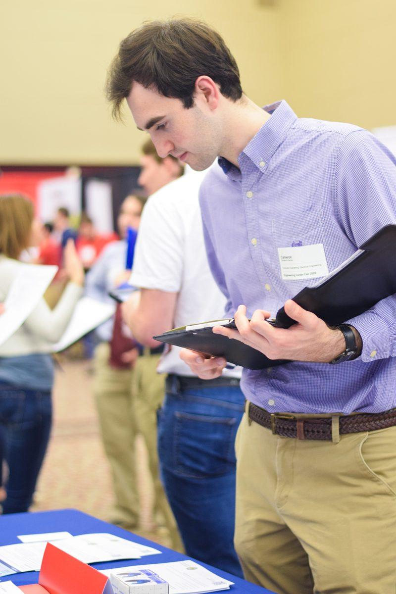 Cameron Dennis, a junior in computer engineering looks at information at the booth of a possible future employer at the Engineering Career Fair on Wednesday, Feb. 5, 2020 at the McKimmon Center. The Career Fair helps students and attendees network with companies looking for employees and interns.