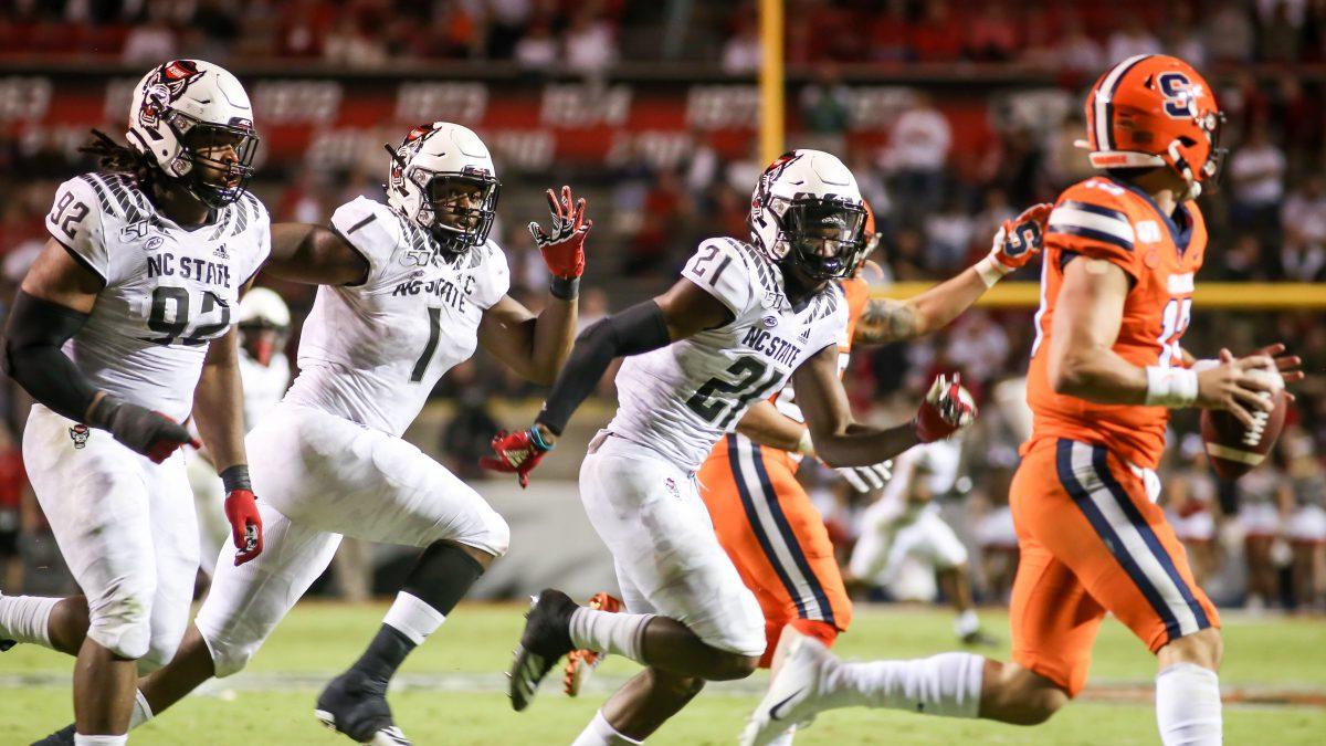 NC State defenders Larrell Murchison, James Smith-Williams and Stephen Griffin, chase down Syracuse quarterback Tommy DeVito, leading to an incomplete pass. NC State hosted the Syracuse Orange on Thursday, October 10, 2019. NC State won the game 16-10. DeVito was sacked 8 times during the game, losing 52 yards.