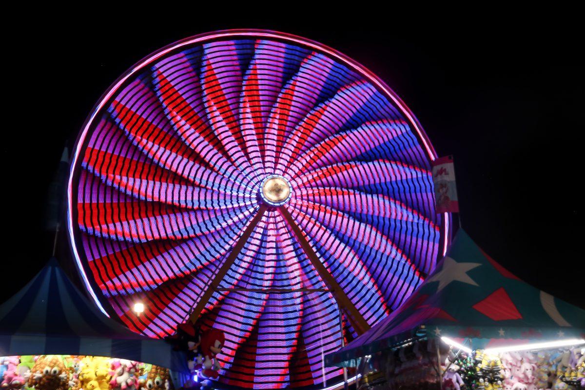 The ferris wheel displays a constantly shifting array of colors as it spins in front of game booths filled with prizes at the NC State Fair on Saturday, October 19, 2019.