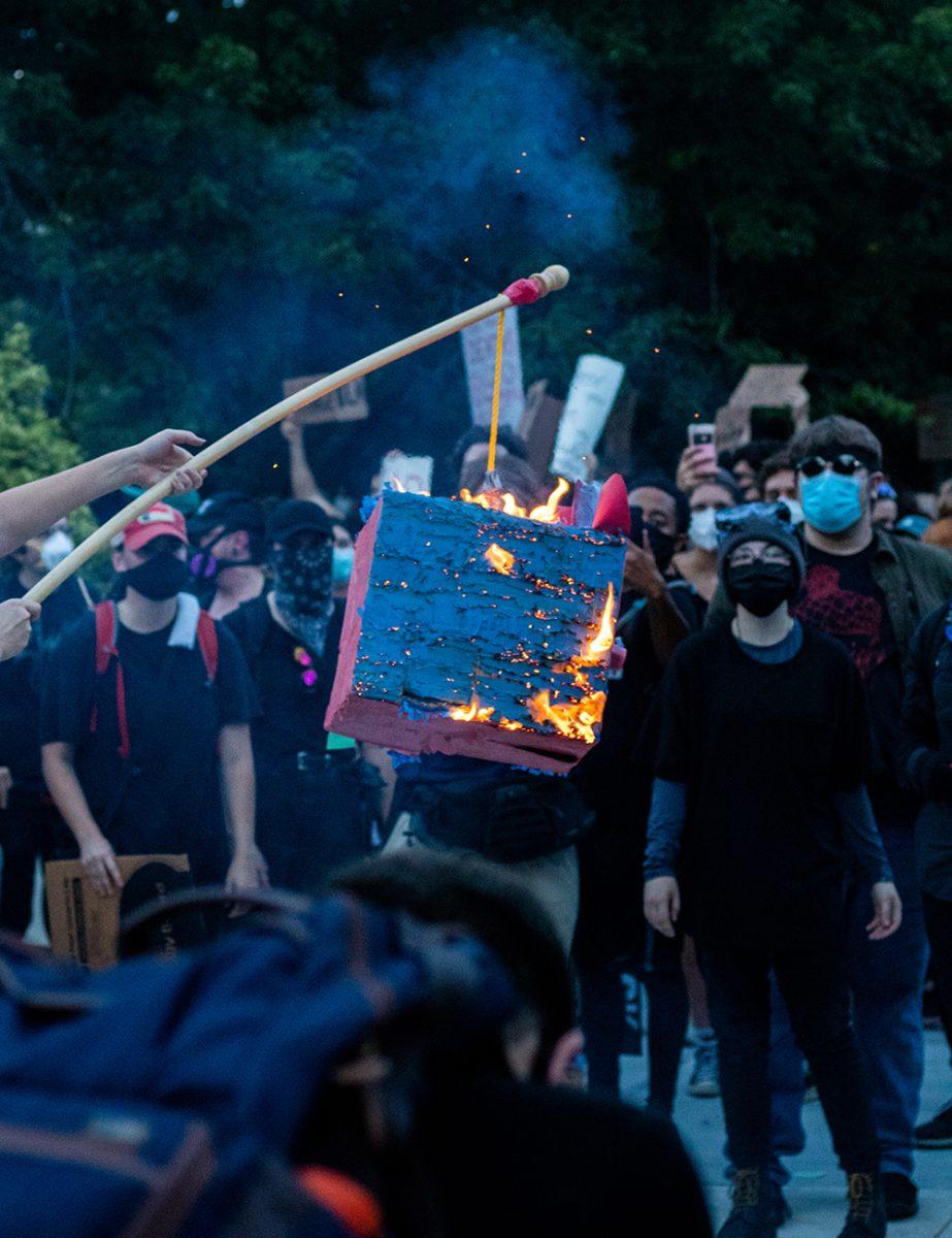 Protesters watch on as a pi&#241;ata is set aflame in front of the North Carolina Legislative Building in downtown Raleigh on Friday, Aug. 28, 2020.