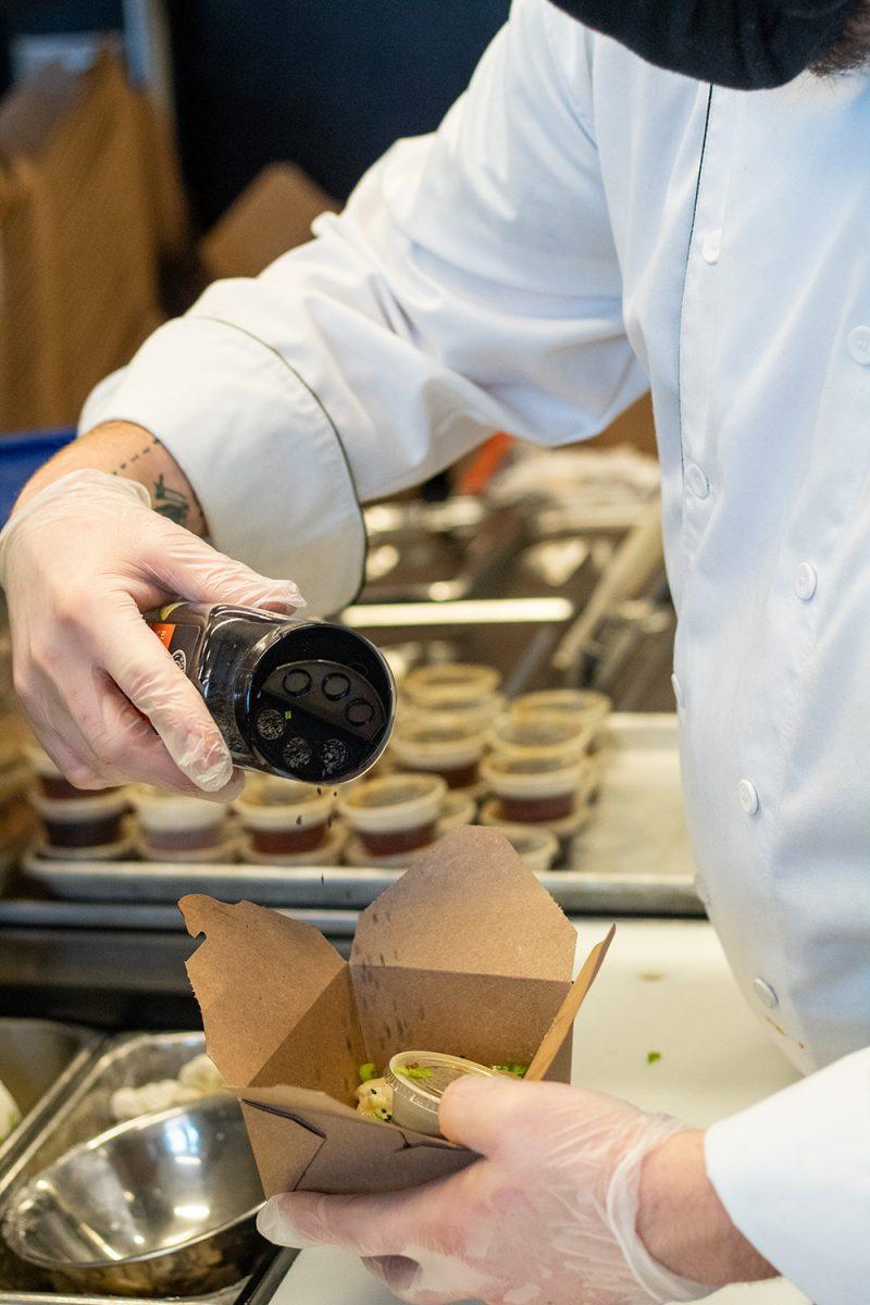 Hector Vega Jr, the Executive Sous-Chef of 1887 Bistro, pours pepper on an order in a to-go box in the kitchen of 1887 Bistro on Wednesday, Sept. 23, 2020.