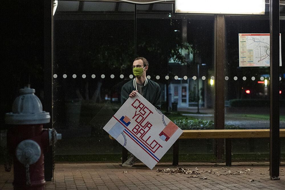Austin Dunlow, arts and entertainment editor for Technician, sits alone on a bench holding a sign outside of Witherspoon Student Center on Tuesday, Oct. 13th, 2020.