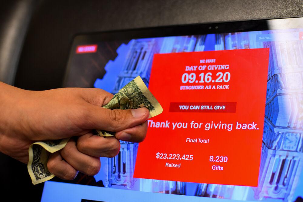 A crunched up dollar bill is held in front of the Day of Giving website on Thursday, Sept. 24. 2020.