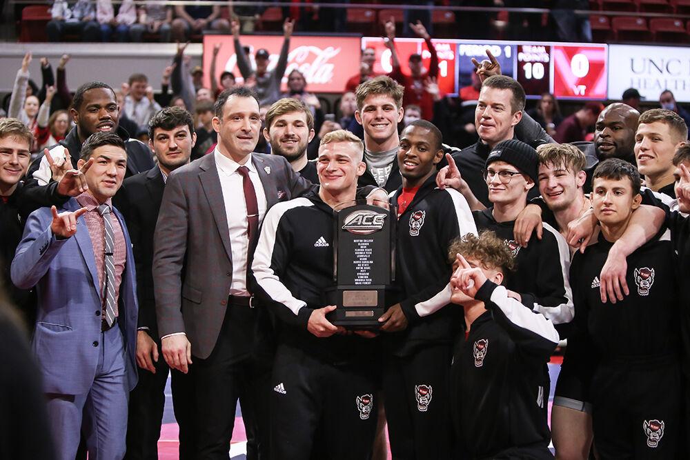 NC State's players and coaches pose with the ACC Championship trophy in front of fans. NC State beat Virginia Tech 21-10 in a wrestling match in Reynolds Coliseum on Sunday, Feb. 20, 2022.