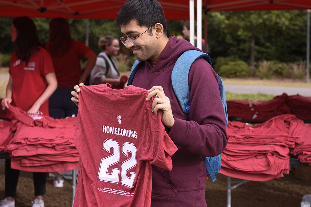 Rohan Sinha, a graduate student studying computer science, smiles while holding his new NC State Homecoming shirt at the Red and White Week Kickoff on Monday, Oct. 31, 2022 at Stafford Commons. The NC State Alumni Association handed out free shirts at the Red and White Week Kickoff for NC State&#8217;s homecoming week.