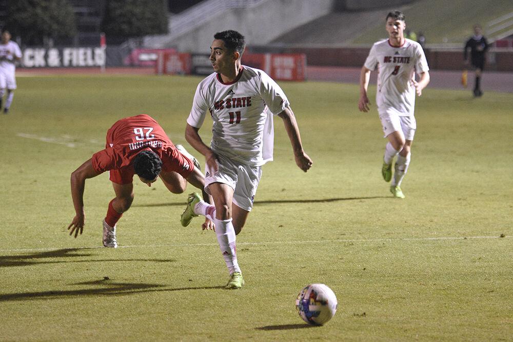 Sophomore forward Henrique Santos dribbles the ball past a fallen Radford defender during the match against Radford on Tuesday, Oct.&#160;25, 2022 at Dail Soccer Field. The Wolfpack won 2-0.