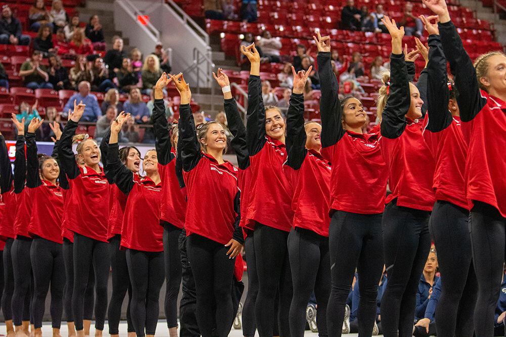 The NC State gymnastics team hold up a "wolfie" after hearing the final scores for the meet against Pitt and George Washington at Reynolds Coliseum on Saturday, Jan. 21, 2023. NC State beat Pitt and George Washington with an overall score of 196.650.
